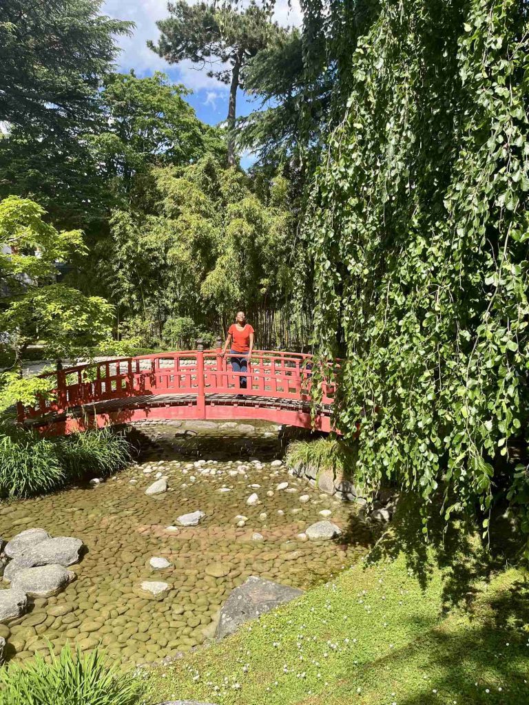 The author standing on the iconic red bridge at Musée Albert-Kahn, surrounded by lush greenery in the Japanese Garden. 