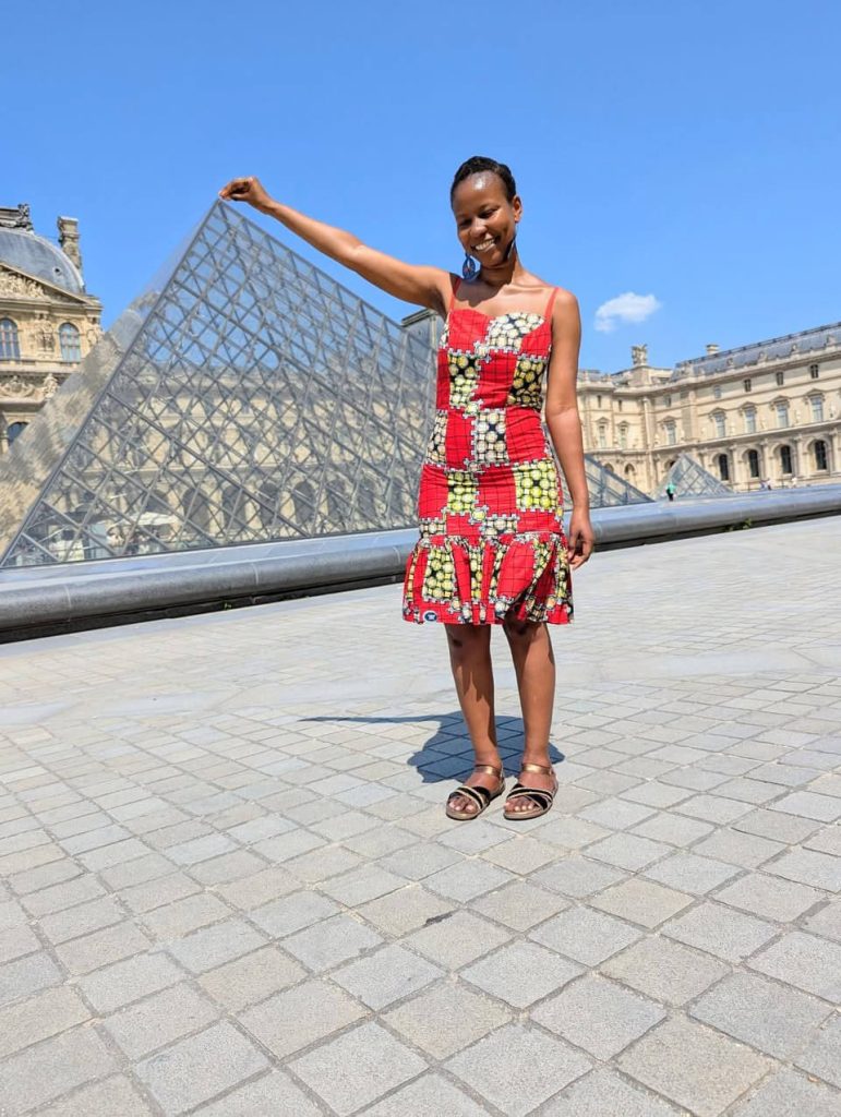 The author posing cheerfully in front of the modern glass Louvre Pyramids, one of the places to visit for free in Paris.